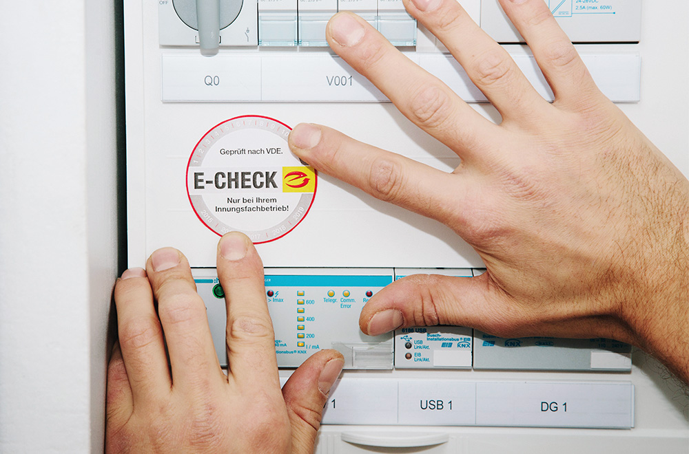 Person klebt eine E-CHECK-Plakette in einen Schaltschrank.
